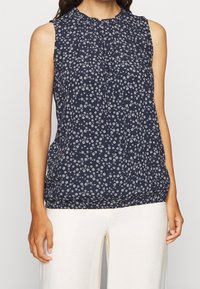 Marinblus utan ärmar med vitt blommönster, samlad halsringning och elastisk nederkant. Lättviktig och andningsbar tyg som är lämplig för varmt väder.