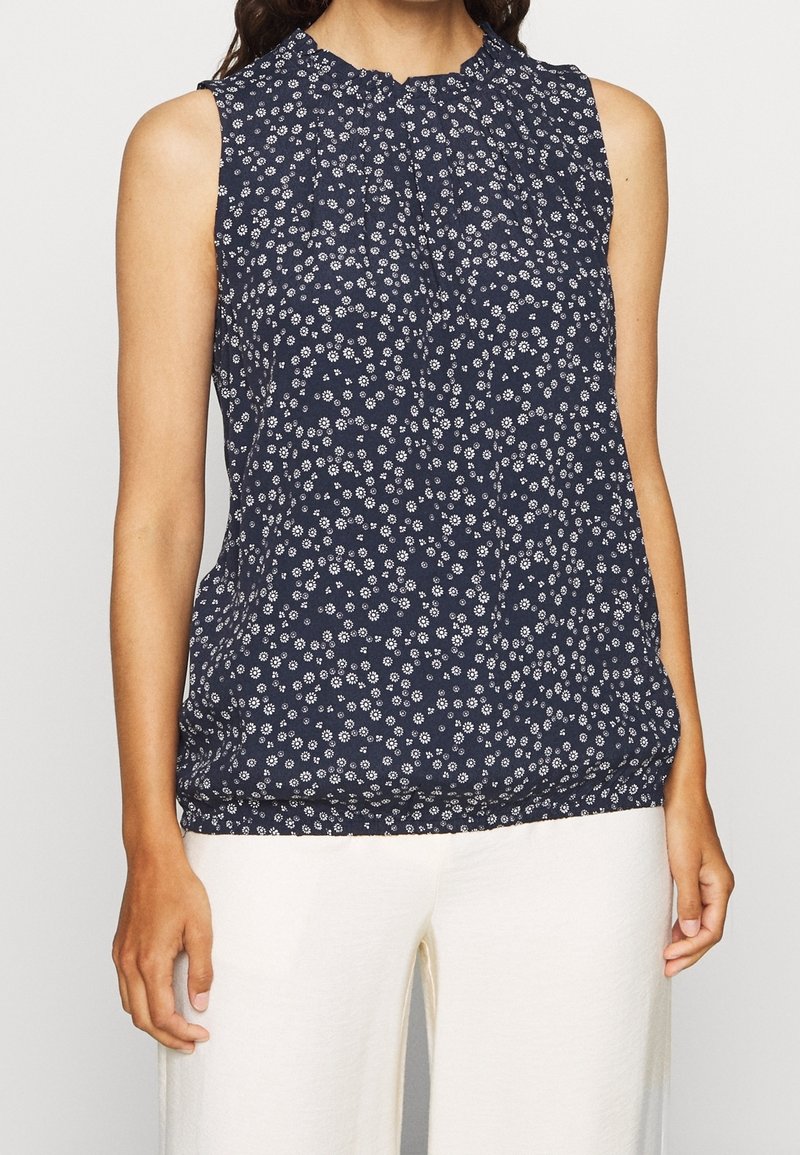 Marinblus utan ärmar med vitt blommönster, samlad halsringning och elastisk nederkant. Lättviktig och andningsbar tyg som är lämplig för varmt väder.