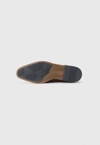 Semelle de chaussure avec une base en caoutchouc marron texturé et un talon noir solide. Présente un motif de bande de roulement pour une meilleure adhérence.