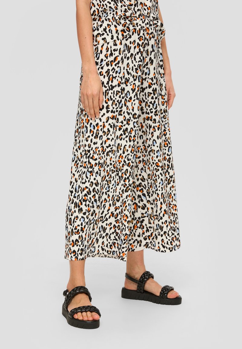 Spódnica midi w panterkę w kolorze kremowym, z czarnymi, pomarańczowymi i brązowymi plamami; zestawiona z czarnymi plecionymi sandałami na teksturowanej podeszwie.