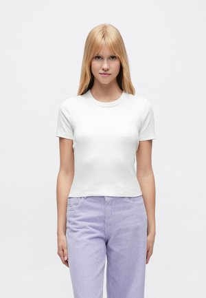 T-shirt blanc ajusté à manches courtes avec un col rond, associé à un pantalon en velours côtelé violet clair. Texture lisse, design minimaliste.