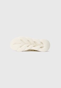 Semelle de chaussure blanche avec un motif de semelle texturé en forme de feuille et des détails de grip sur un fond blanc uni.