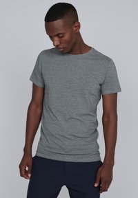 Camiseta gris de manga corta fabricada en una mezcla de algodón, con un cuello redondo clásico y una silueta ajustada. Sin patrones ni gráficos visibles.