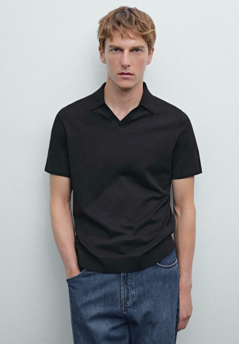 Černá polokošile s krátkým rukávem a véčkovým výstřihem, hladká textura a jednobarevný design, v kombinaci s světlými modrými džíny.