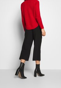 Röd texturerad tröja med långa ärmar, i kombination med svarta uppklippta byxor och svarta högklackade ankelstövlar.