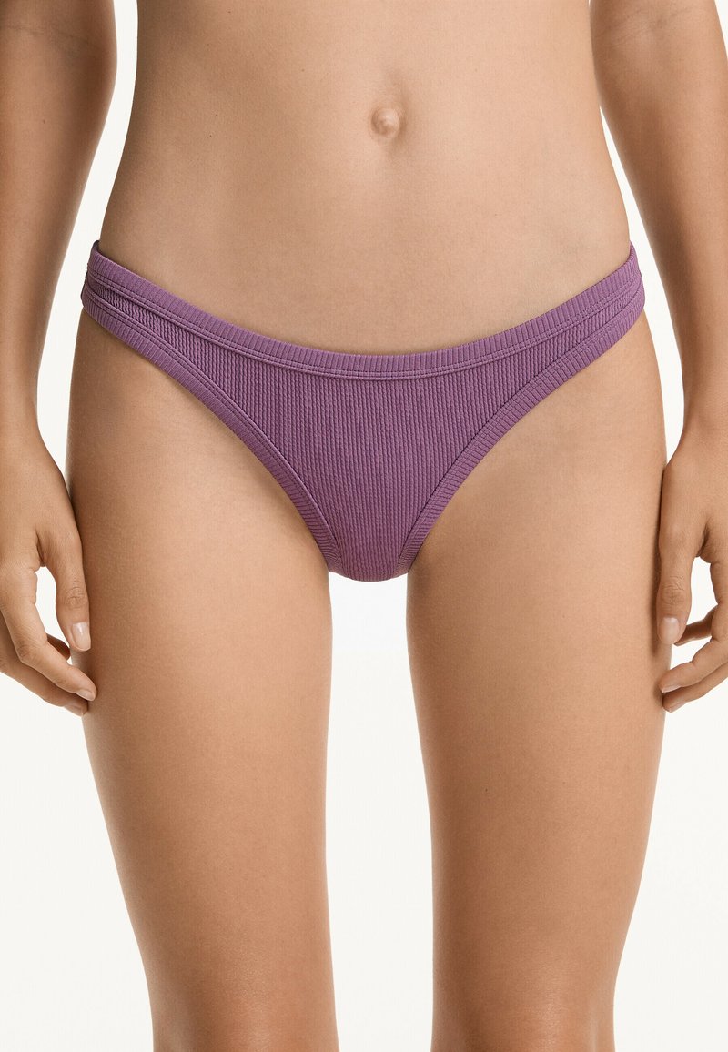 Ribbad bikiniunderdel i en djup lila färg. Har en lågt skuren design med tunna sidostaplar. Materialet verkar vara elastiskt och texturerat.