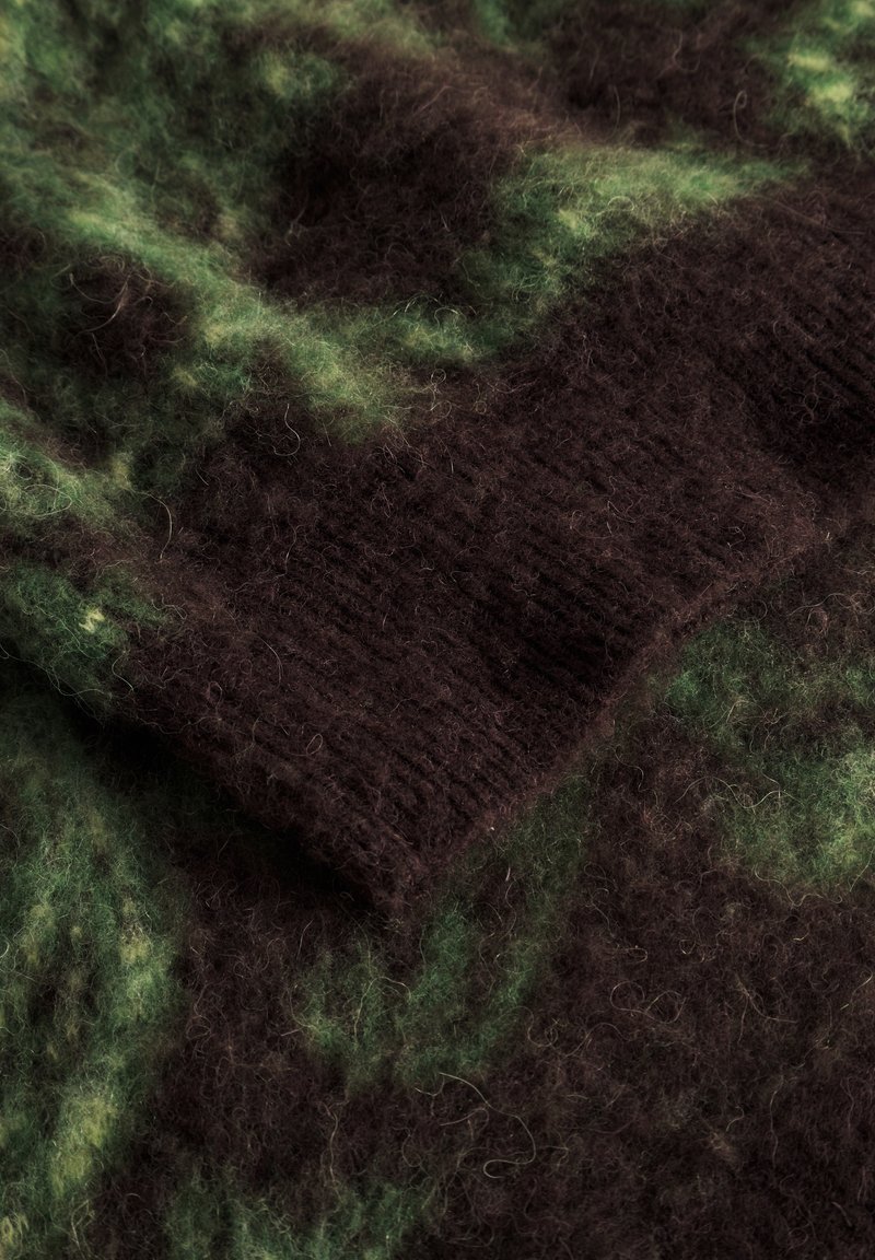 Tissu en laine texturé dans des nuances de vert foncé et de marron, présentant une surface douce et duveteuse avec une section tricotée à côtes. Accents de fibres mélangées visibles.