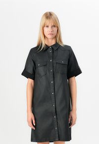 Abito camicia in denim nero con maniche corte, chiusura frontale a bottoni, due tasche sul petto e orlo leggermente svasato. Texture liscia.