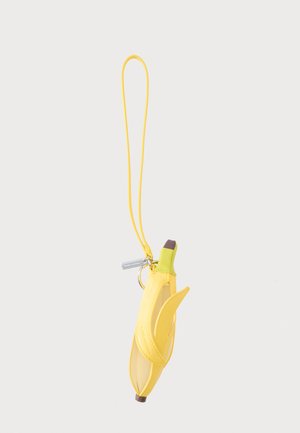 Gelbe bananenförmige Tasche mit Schalen-Detail und Handgelenksriemen vor einem einfarbigen hellgrauen Hintergrund.