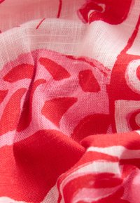 Tessuto a motivi rossi e rosa con una texture leggera e trasparente, che mostra un drappeggio morbido e fluido e elementi di design astratti.