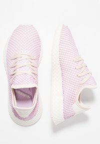 Pár světle růžových síťovaných tenisek Adidas s bílými podrážkami a tkaničkami, zobrazené z vrchu a z boku na bílém pozadí.