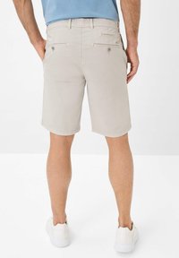 Licht beige shorts met een gladde textuur, voorzien van twee achterzakken met knopen en riemlussen, gecombineerd met witte instappers.