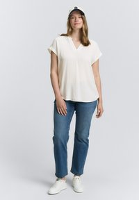 Vit v-ringad blus med korta, uppvikta ärmar, kombinerat med blå raka jeans. En ljusbeige och marinblå keps fulländar outfiten. Vita sneakers.
