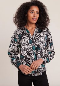 Knoop-up blouse in een zwart, wit en teal bloemenpatroon, met lange mouwen, een kraag en een ontspannen pasvorm. Glad textuur van de stof.