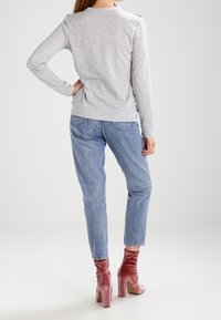 Top grigio a maniche lunghe con dettagli sulle spalle, abbinato a jeans azzurri chiari e stivali con tacco in velluto rosa. Tessuto morbido e vestibilità casual.