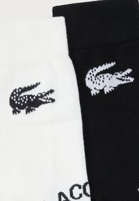 Chaussettes noires et blanches avec des logos crocodile contrastants tricotés près des bords supérieurs de chaque chaussette.