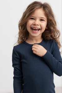 Sötétkék bordázott hosszú ujjú felső, kerek nyakkivágással és apró gombdísszel elöl, egy göndör barna hajú gyermek viseli.