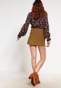 Sort blomsterbluse med lange ærmer, parret med en kort olivenfløjlsskirt og brune ankelstøvler.