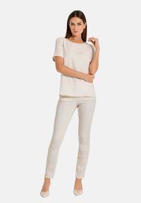 Hellbeige Bluse mit rundem Ausschnitt und kurzen Ärmeln, kombiniert mit taillierten, cremefarbenen Hosen. Beide Kleidungsstücke haben eine glatte Textur.