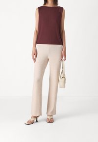 Ribbad maroon ärmlös topp i kombination med beige ribbad vida byxor. Modellen håller en liten krämfärgad väska och har på sig strappy beige sandaler.