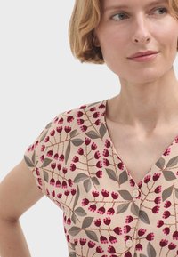 Camicia button-up con maniche corte, caratterizzata da un motivo floreale in rosa e bordeaux su uno sfondo beige chiaro. Design con scollatura a V.