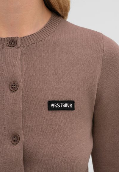 Cardigan marron boutonné avec col côtelé et un patch rectangulaire noir sur la poitrine portant l'inscription "YASTBNHA."