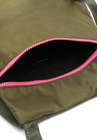 Sac vert olive avec une fermeture éclair rose vif et un intérieur noir ; doté d'une seule poignée et d'un tissu doux et texturé. Poche zippée visible.