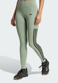Leggings sportivi verdi a vita alta con strisce laterali nere, texture liscia e tasca laterale. Abbinate a sneaker nere.