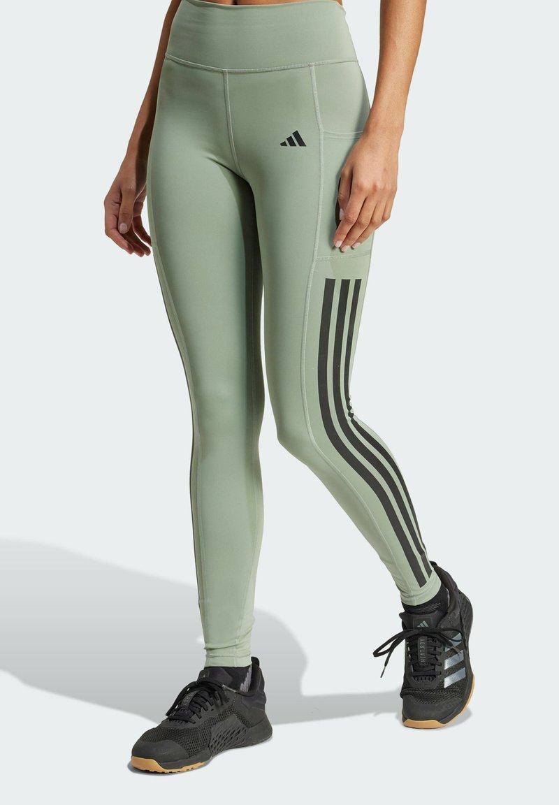Gröna, högmidjade träningsleggings med svarta sidostråk, slät textur och en sidficka. Matchas med svarta sneakers.