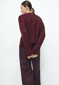 Maglione lavorato a maglia color bordeaux con vestibilità comoda, scollo a coste e spalle scese, abbinato a pantaloni coordinati dalla vestibilità ampia.