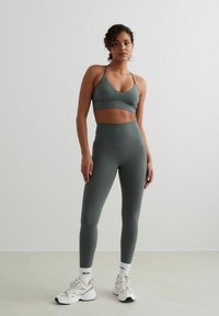 Sportbeha en legging set in olijfgroen, gemaakt van rekbaar materiaal. De beha heeft een V-halsontwerp en de leggings hebben een hoge tailleband.