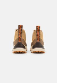 Hochschnittige Sneaker aus beigefarbenem Wildleder und braunem Synthetikmaterial, mit einem auffälligen "GANT"-Logo an der Ferse und einer strukturierten Gummisohle.
