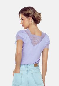 Liliowa koszulka z koronkowymi akcentami przy dekolcie i rękawach, zestawiona z jasnoniebieskimi szortami z wysokim stanem, prezentującymi luźny fason.