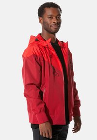 Rote wasserdichte Jacke mit Kapuze, ausgestattet mit einer Mischung aus Texturen, elastischen Bündchen und vorderseitigen Reißverschlusstaschen. Leicht und atmungsaktiv.