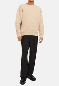 Felpa beige a girocollo realizzata in tessuto morbido, abbinata a pantaloni neri su misura e scarpe nere. L'outfit presenta una vestibilità rilassata e un design classico.