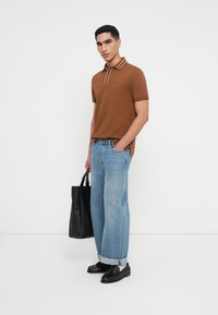 Brūna polo krekla ar svītrainu apkakli, apvienots ar gaiši ziliem platajiem džinsiem. Modelis tur melnu rokassomu un valkā melnas kurpes.