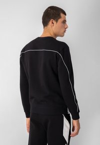Sudadera negra de cuello redondo, con ribetes blancos a lo largo de las costuras de los hombros y un dobladillo de canalé. Tejido suave con un corte relajado.