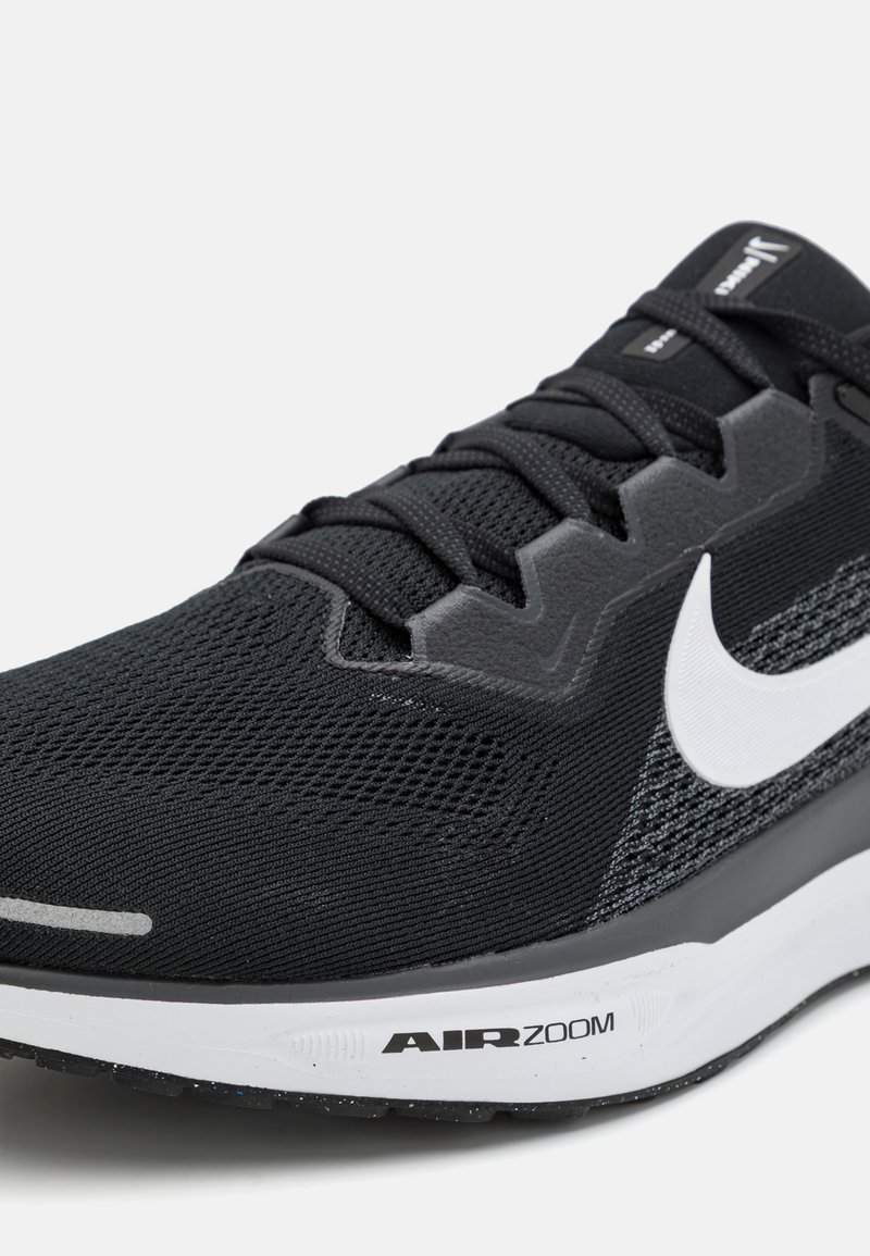 Zapatilla deportiva negra con parte superior de malla texturizada, acentos grises, logo de Nike en blanco y suela acolchada AIRZOOM. Vista lateral.