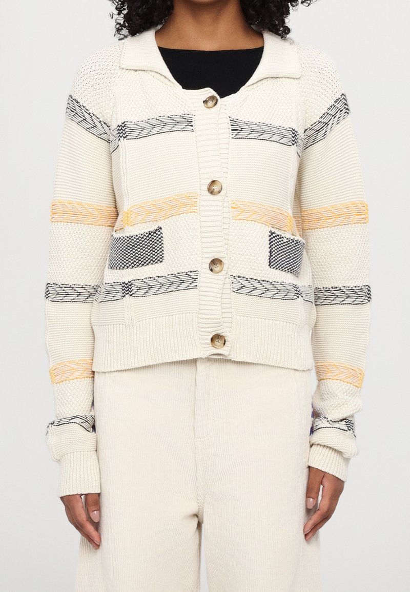 Kremowy kardigan z kołnierzykiem, ozdobiony poziomymi paskami w żółtym, czarnym i niebieskim wzorze, z dużymi guzikami z przodu.