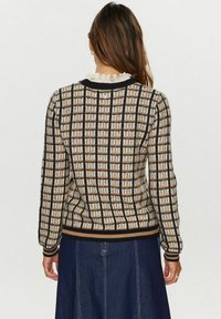 Pull en maille à motif à carreaux beige et marron avec accents noirs, avec manches longues, encolure arrondie et ourlet côtelé.