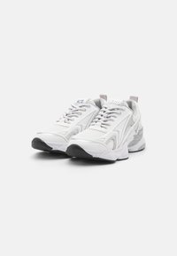 Chaussures de sport blanches avec une tige en mesh, ornées d'accents gris, une semelle épaisse et rembourrée, ainsi que des lacets. Détails texturés uniques sur les côtés.