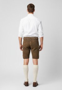 Bruna lädershorts med en texturerad yta, i kombination med krämfärgade knästrumpor och bruna skor, sedd bakifrån.