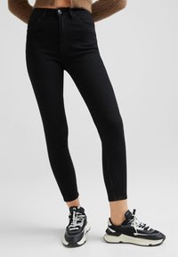 Jeans negros de cintura alta con un ajuste slim y tejido elástico; combinados con zapatillas negras y blancas con una suela gruesa y cordones.