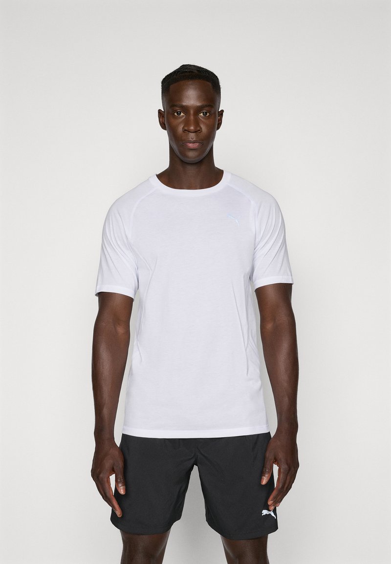 Camiseta atlética blanca de manga corta con cuello redondo y logotipo azul claro en el pecho, combinada con pantalones cortos negros. Textura suave.