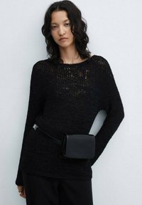 Černý pletený svetr s volným střihem a dlouhými rukávy, doplněný malou černou koženou ledvinkou. Jednobarevný, texturovaný materiál.
