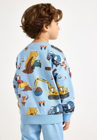 Jasnoniebieska bluza z nadrukami kolorowych pojazdów budowlanych, w tym ciężarówek i koparek. Ściągacze na rękawach i u dołu. Miękka faktura materiału.