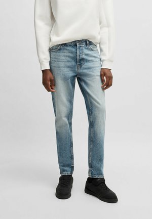 Jeans in denim chiaro con una finitura sbiadita, vestibilità dritta, cinque tasche e passanti per cintura, abbinati a una felpa bianca e sneakers nere.