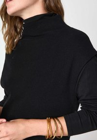 Indumento nero a coste con collo alto e maniche corte, caratterizzato da una texture liscia. Accentuato da bracciali metallici sui polsi.
