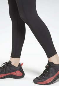 Svart atletisk leggings med en slät yta och en figurnära design. Kombinerat med svarta sneakers med röda detaljer och snörning.