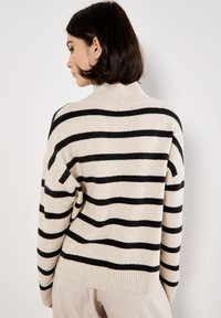 Maglione beige con righe orizzontali nere, caratterizzato da un alto colletto e polsini a coste. Morbido al tatto e vestibilità comoda.